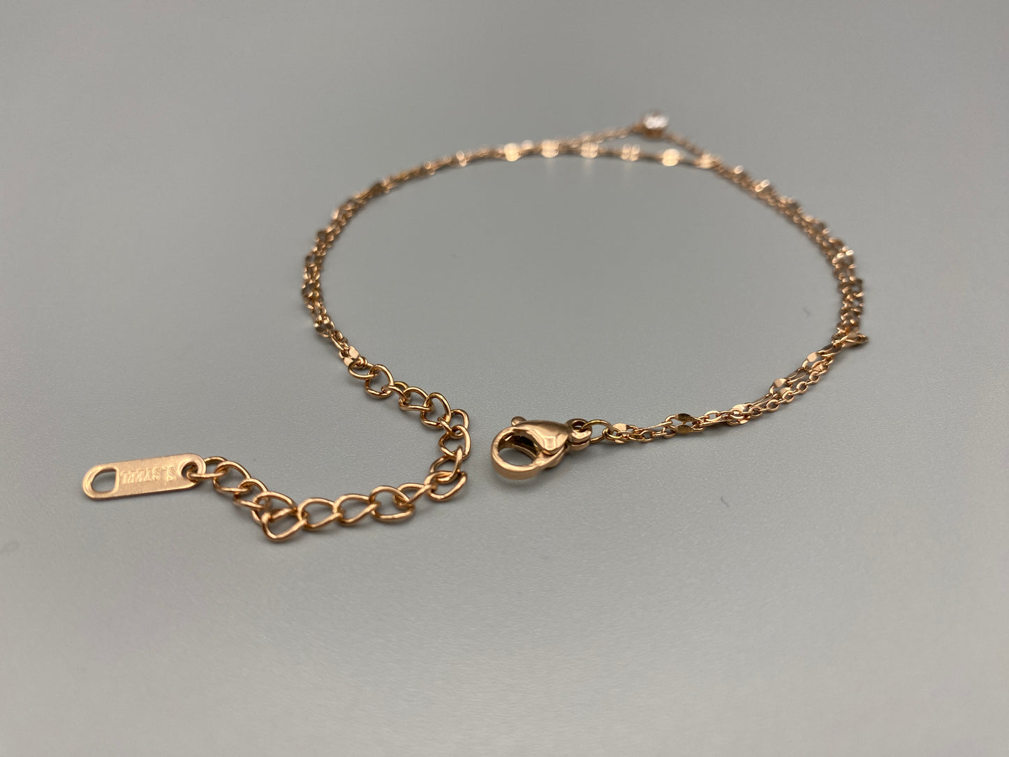 "Aurora Twin Chain Bracelet in rose gold features a sophisticated twin chain design adorned with zirconia gemstones. It is waterproof and measures 18 cm with a 3 cm extender for an adjustable fit."