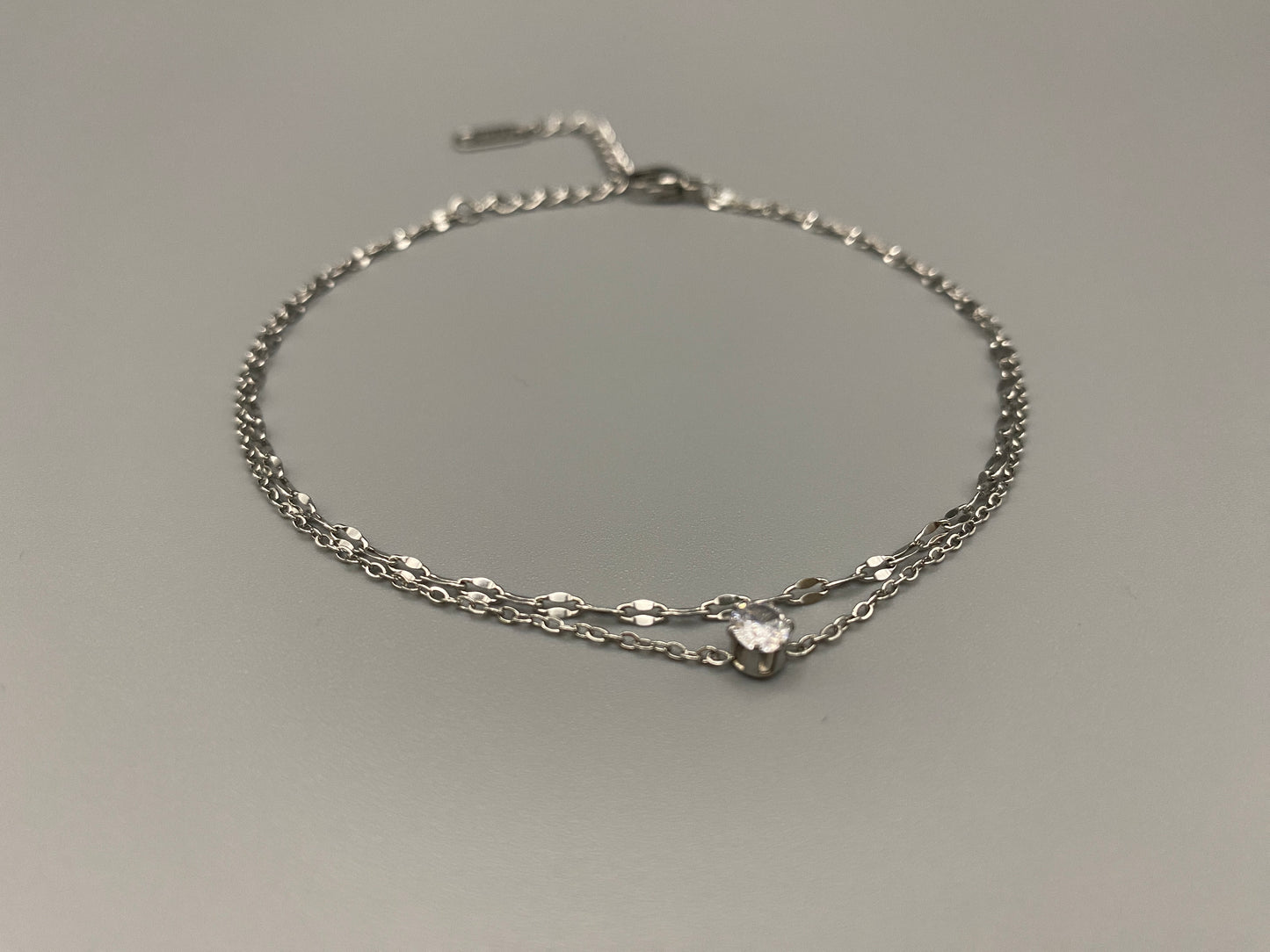 “Aurora Twin Chain Bracelet in silver with a sophisticated twin chain design, adorned with sparkling zirconia gemstones. Waterproof and measures 18 cm with a 3 cm extender for adjustable fit.”