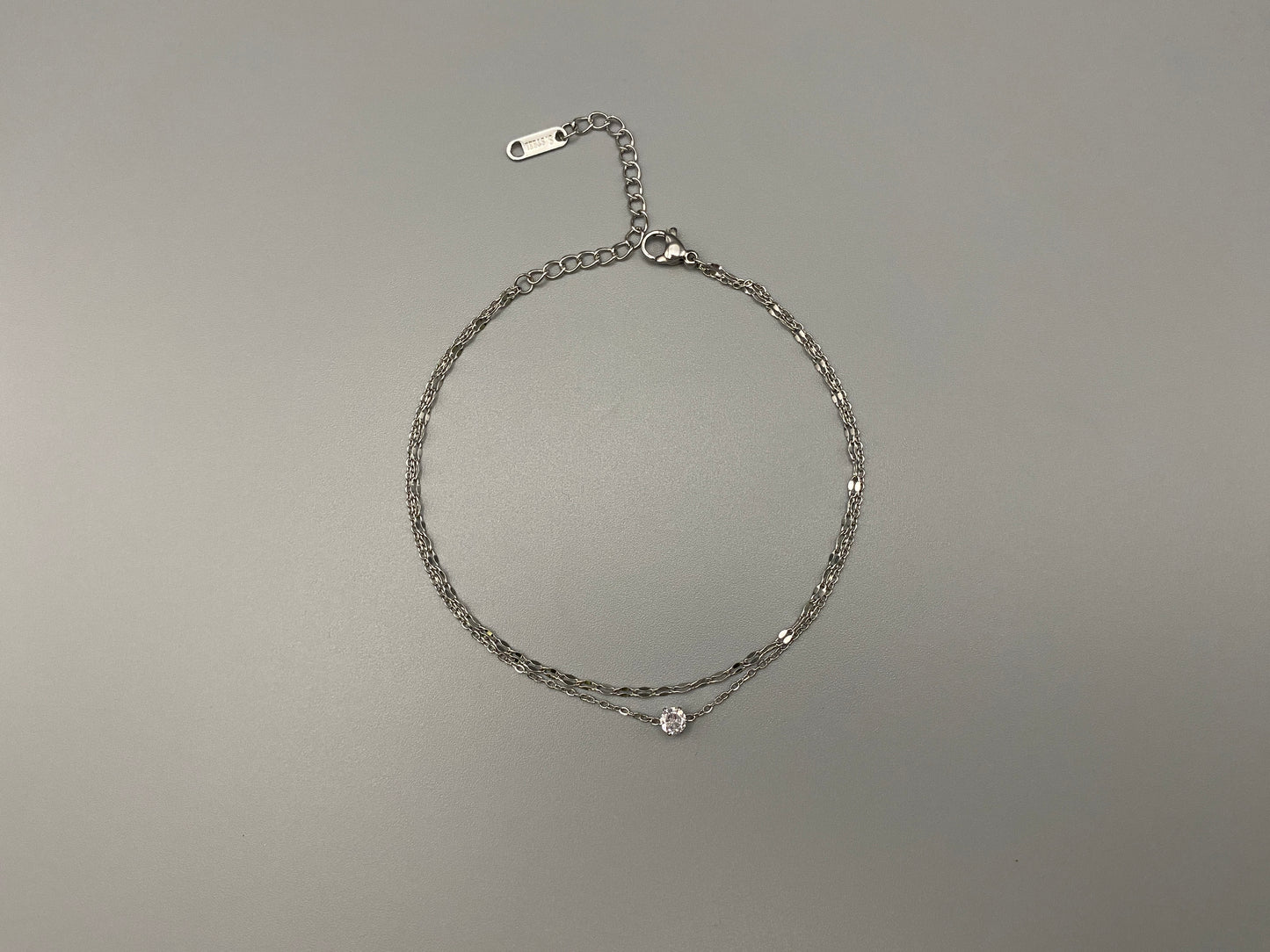 “Aurora Twin Chain Bracelet in silver with a sophisticated twin chain design, adorned with sparkling zirconia gemstones. Waterproof and measures 18 cm with a 3 cm extender for adjustable fit.”