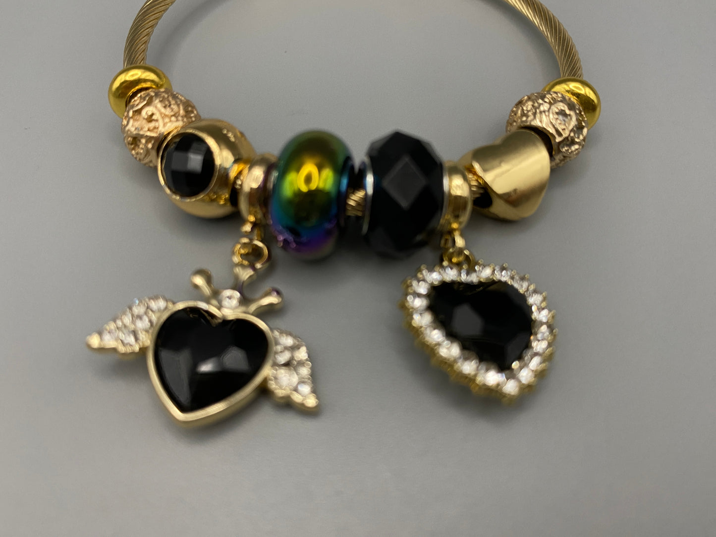 “Belle Black Charm Bracelet with gold-plated finish, featuring heart-cut crystals and rhinestones. Made from durable stainless steel with playful charms and micro insert inlay technology.”