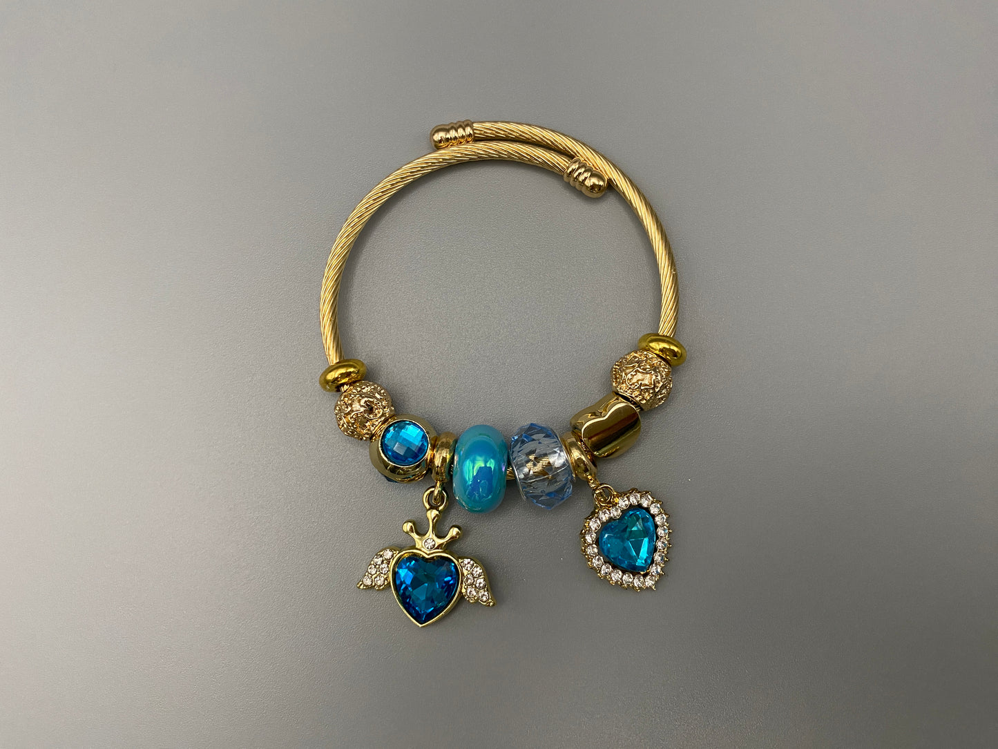 “Belle Blue Charm Bracelet with gold-plated finish, featuring heart-cut crystals and rhinestones. Made from durable stainless steel with playful charms and micro insert inlay technology.”