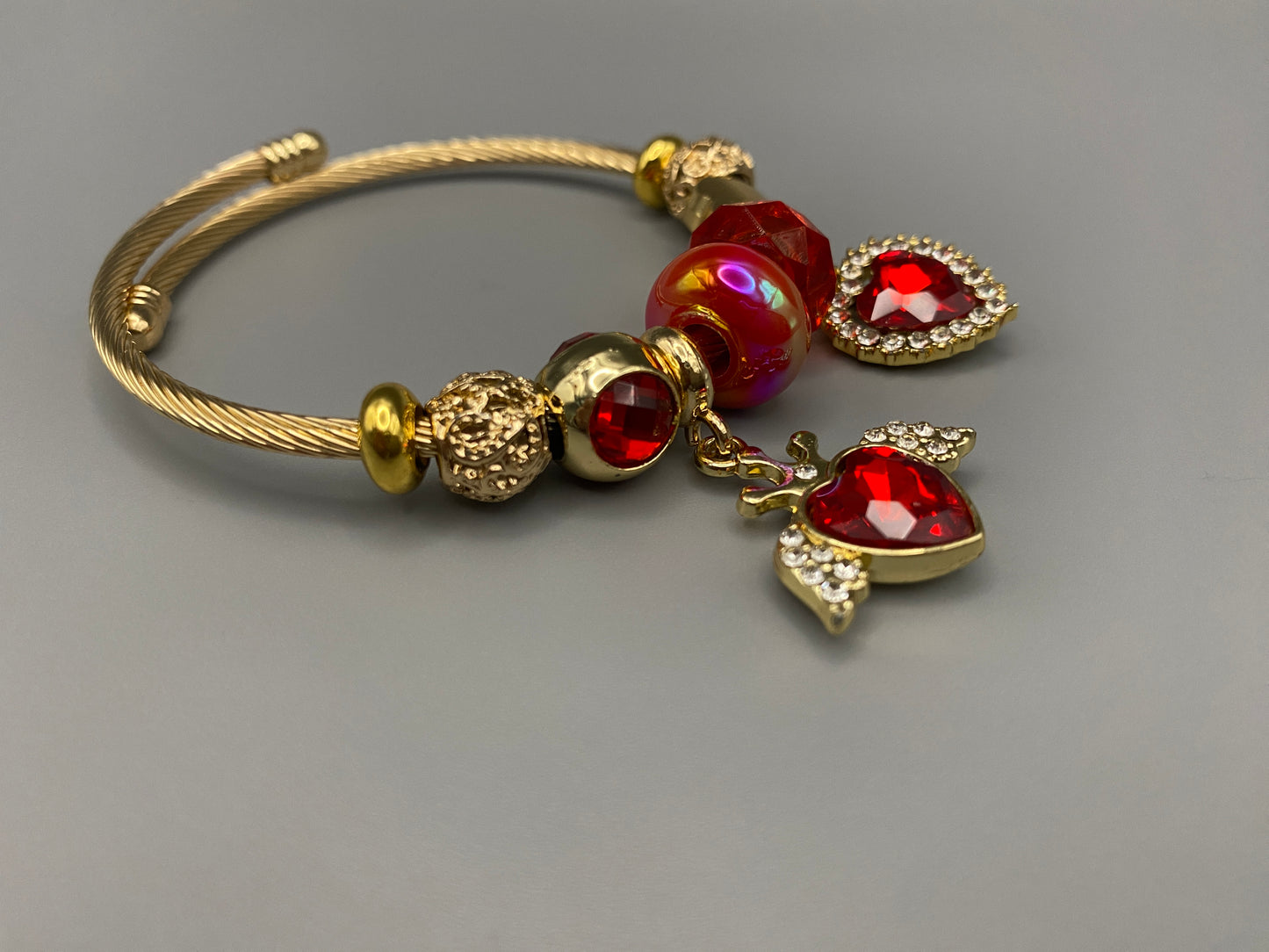 Belle Red Charm Bracelet with gold-plated finish, featuring heart-cut crystals and rhinestones. Made from durable stainless steel with playful charms and micro insert inlay technology.”