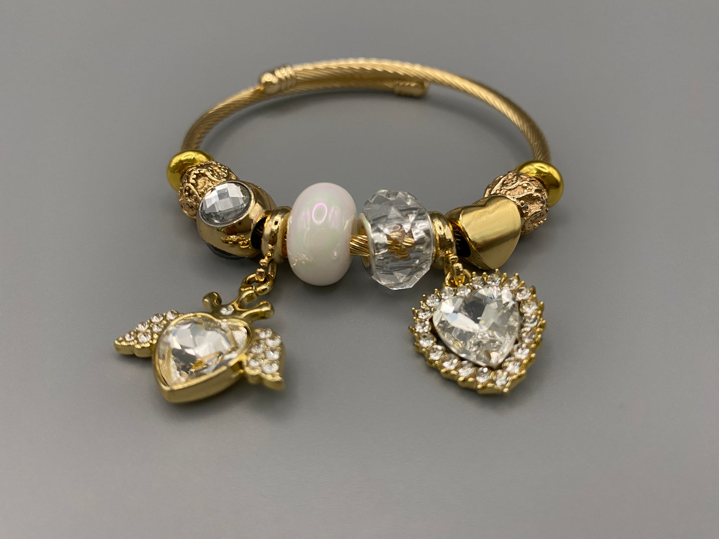“Belle White Charm Bracelet with gold-plated finish, featuring heart-cut crystals and rhinestones. Made from durable stainless steel with playful charms and micro insert inlay technology.”