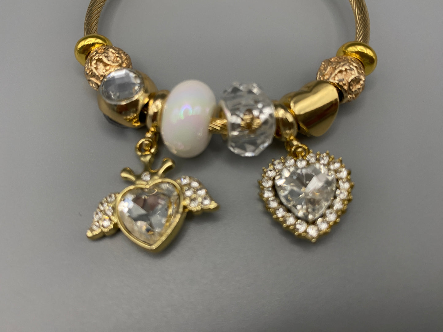 “Belle White Charm Bracelet with gold-plated finish, featuring heart-cut crystals and rhinestones. Made from durable stainless steel with playful charms and micro insert inlay technology.”