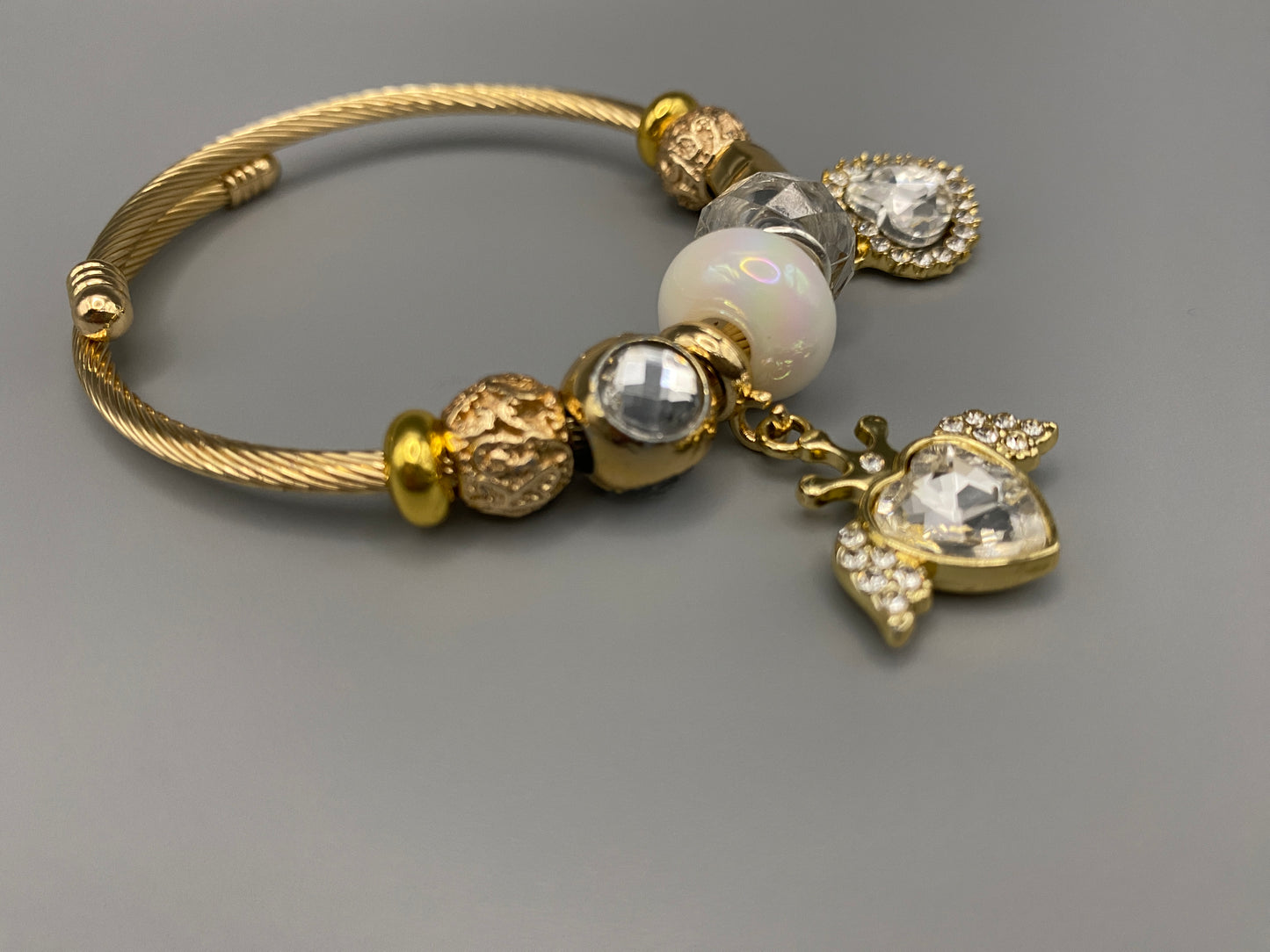 “Belle White Charm Bracelet with gold-plated finish, featuring heart-cut crystals and rhinestones. Made from durable stainless steel with playful charms and micro insert inlay technology.”