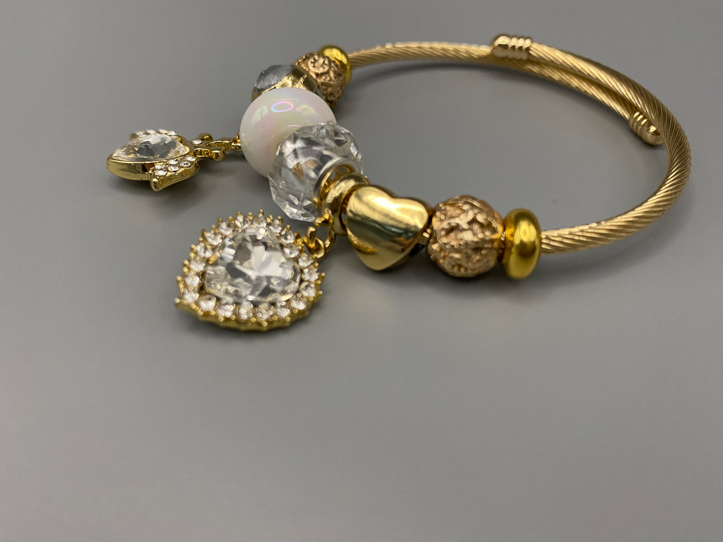“Belle White Charm Bracelet with gold-plated finish, featuring heart-cut crystals and rhinestones. Made from durable stainless steel with playful charms and micro insert inlay technology.”