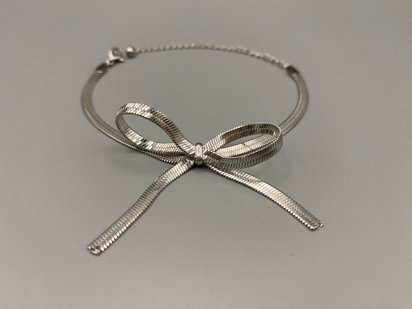 “Celest Angel Bow Bracelet in Silver featuring a delicate bow design, made of stainless steel for durability and tarnish resistance. Measures 18 cm with a 3 cm extender for adjustable fit.”