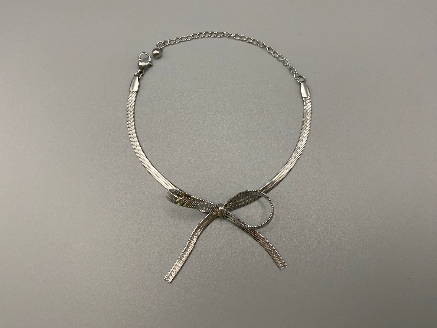 “Celest Angel Bow Bracelet in Silver featuring a delicate bow design, made of stainless steel for durability and tarnish resistance. Measures 18 cm with a 3 cm extender for adjustable fit.”