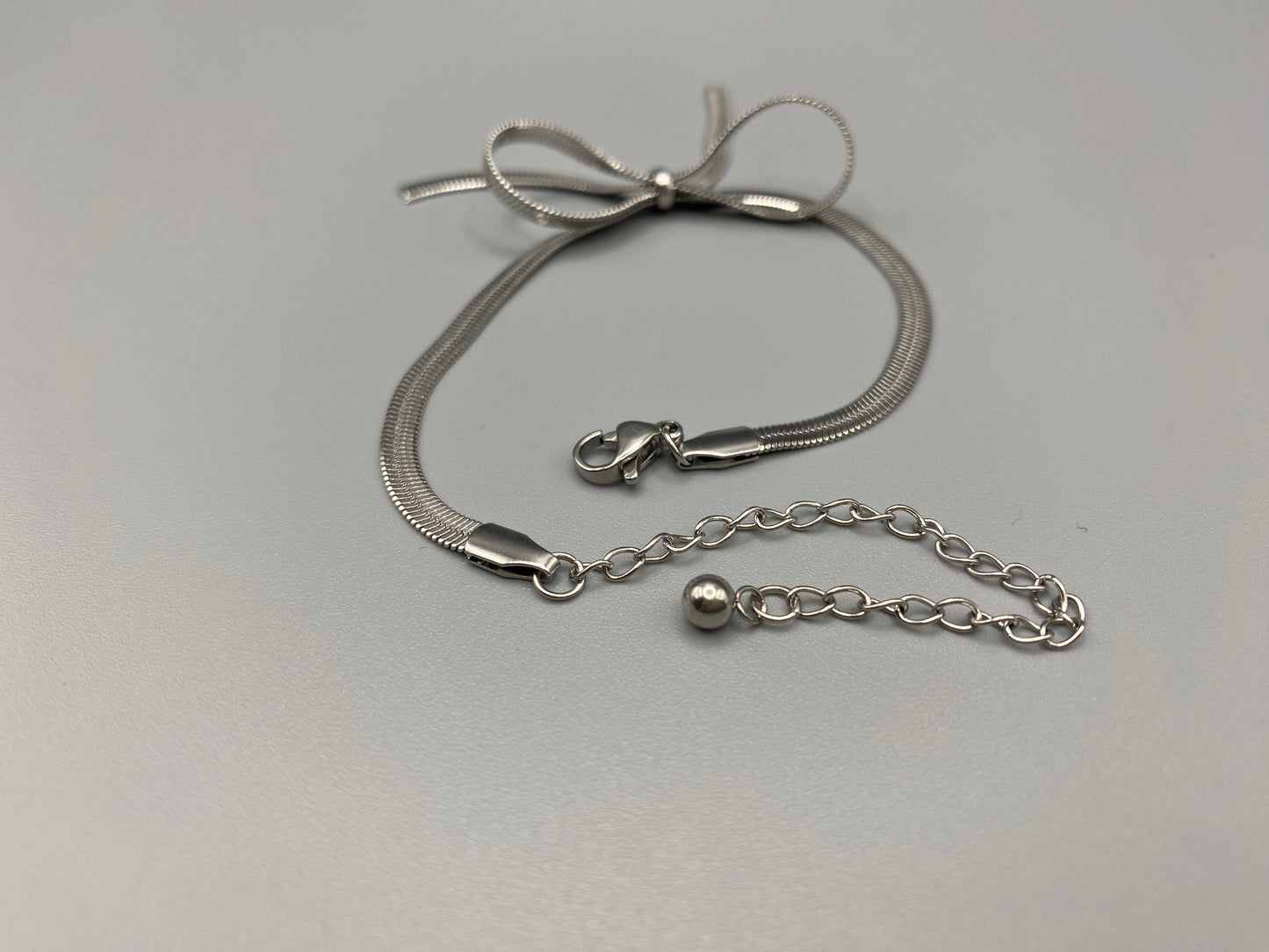 “Celest Angel Bow Bracelet in Silver featuring a delicate bow design, made of stainless steel for durability and tarnish resistance. Measures 18 cm with a 3 cm extender for adjustable fit.”