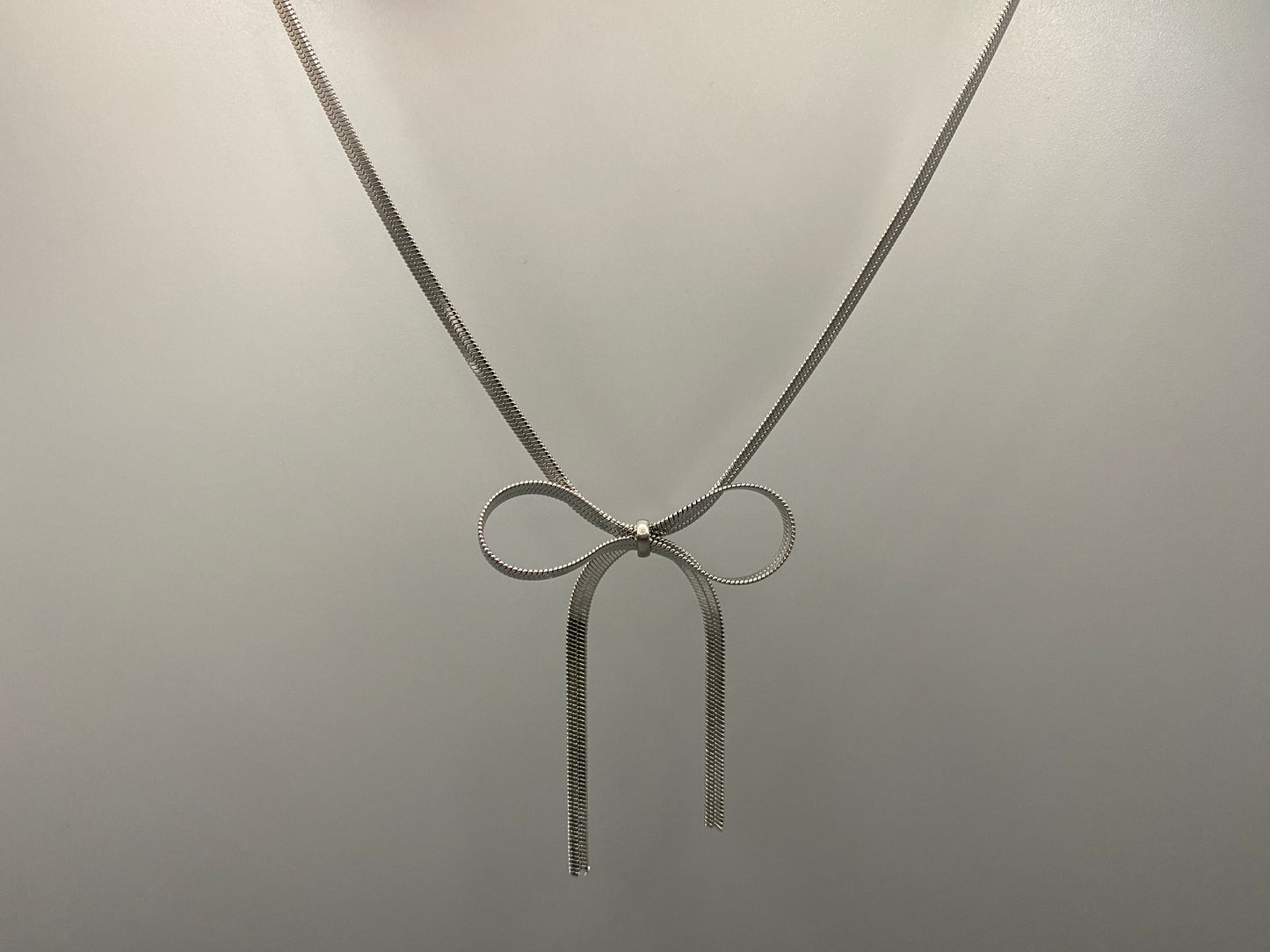 “Celest Angel Bow Pendant Chain in silver with a sophisticated bow pendant design. Made from durable stainless steel, tarnish-free. Measures 35 cm with a 5 cm extender for adjustable fit.”