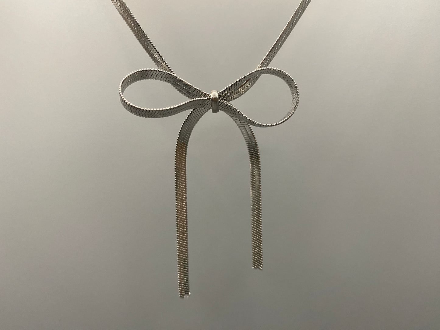 “Celest Angel Bow Pendant Chain in silver with a sophisticated bow pendant design. Made from durable stainless steel, tarnish-free. Measures 35 cm with a 5 cm extender for adjustable fit.”