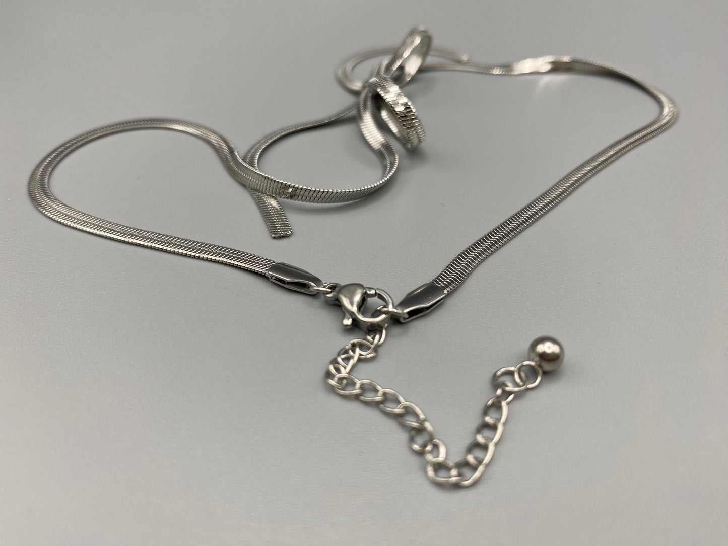 “Celest Angel Bow Pendant Chain in silver with a sophisticated bow pendant design. Made from durable stainless steel, tarnish-free. Measures 35 cm with a 5 cm extender for adjustable fit.”