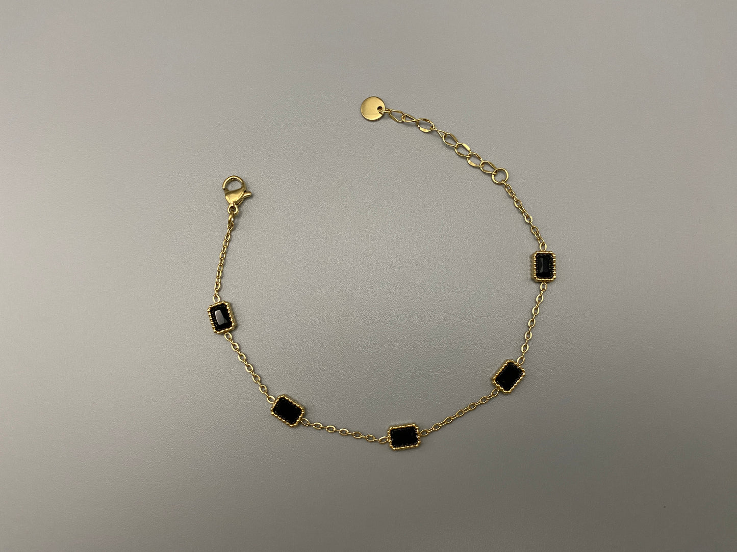 “Clarissa Bracelet in gold with black zircon inset stones, featuring a luxurious gold plating and adjustable length of 17.5 cm with a 2 cm extension. Durable construction ensures long-lasting wear and tarnish resistance.”
