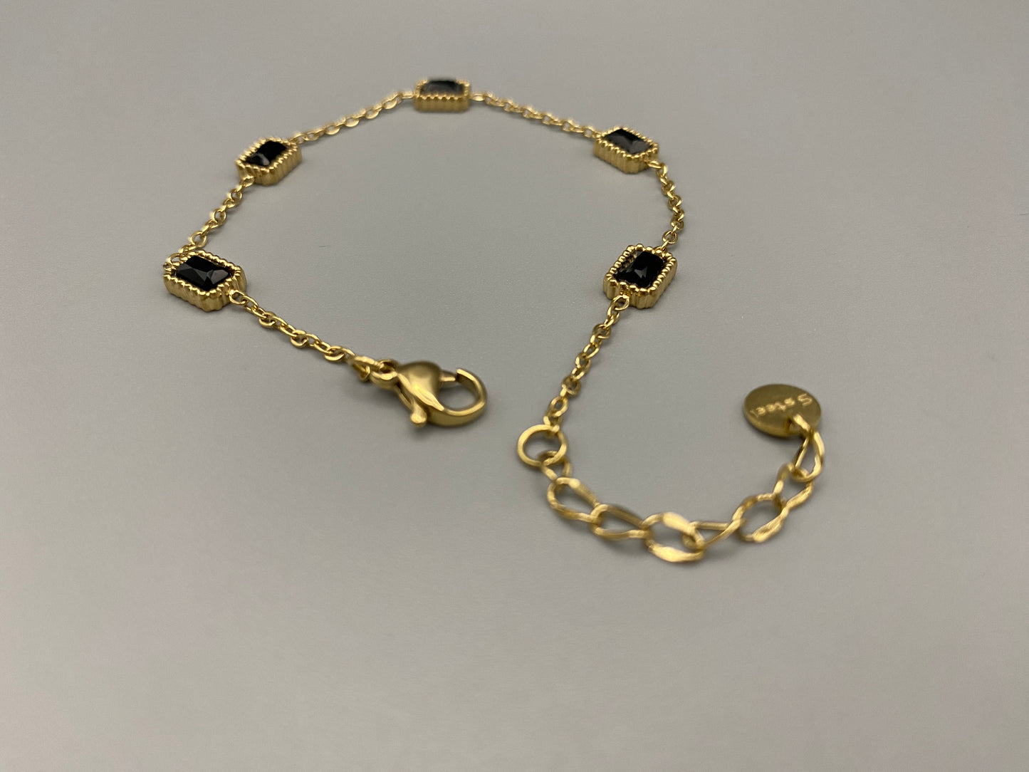 “Clarissa Bracelet in gold with black zircon inset stones, featuring a luxurious gold plating and adjustable length of 17.5 cm with a 2 cm extension. Durable construction ensures long-lasting wear and tarnish resistance.”