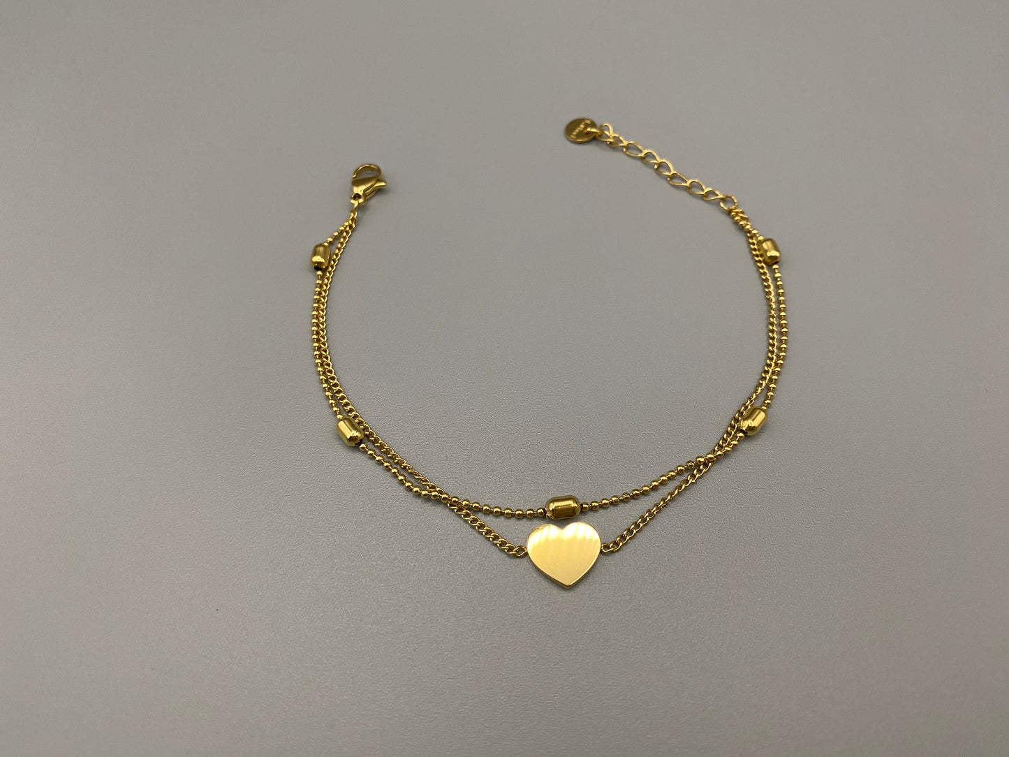 “Cora Twin Chain Heart and Bead Bracelet in gold, featuring a romantic twin chain design with heart and bead accents. 18K gold plated, made from durable titanium steel with PVD plating. Measures 17 cm with a 3 cm extender for adjustable fit.”