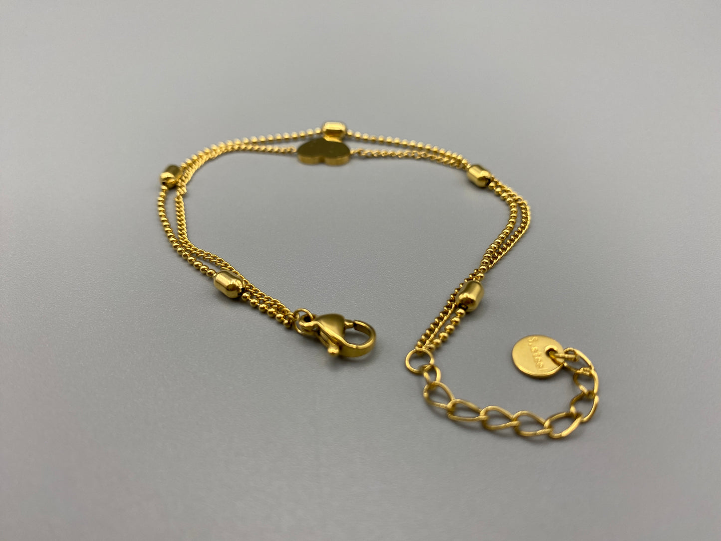 “Cora Twin Chain Heart and Bead Bracelet in gold, featuring a romantic twin chain design with heart and bead accents. 18K gold plated, made from durable titanium steel with PVD plating. Measures 17 cm with a 3 cm extender for adjustable fit.”