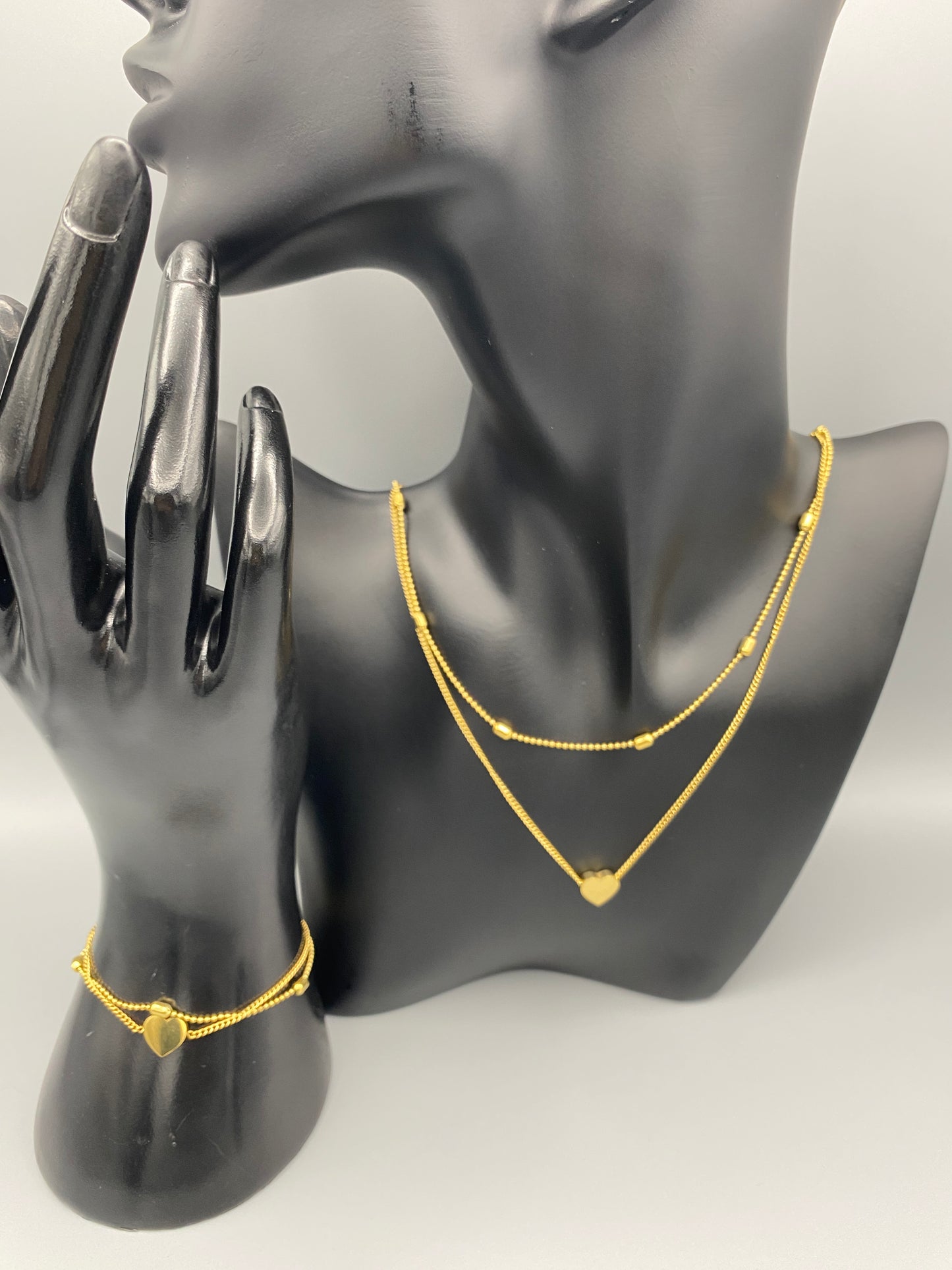 “Cora Twin Chain Heart and Bead Bracelet in gold, featuring a romantic twin chain design with heart and bead accents. 18K gold plated, made from durable titanium steel with PVD plating. Measures 17 cm with a 3 cm extender for adjustable fit.”