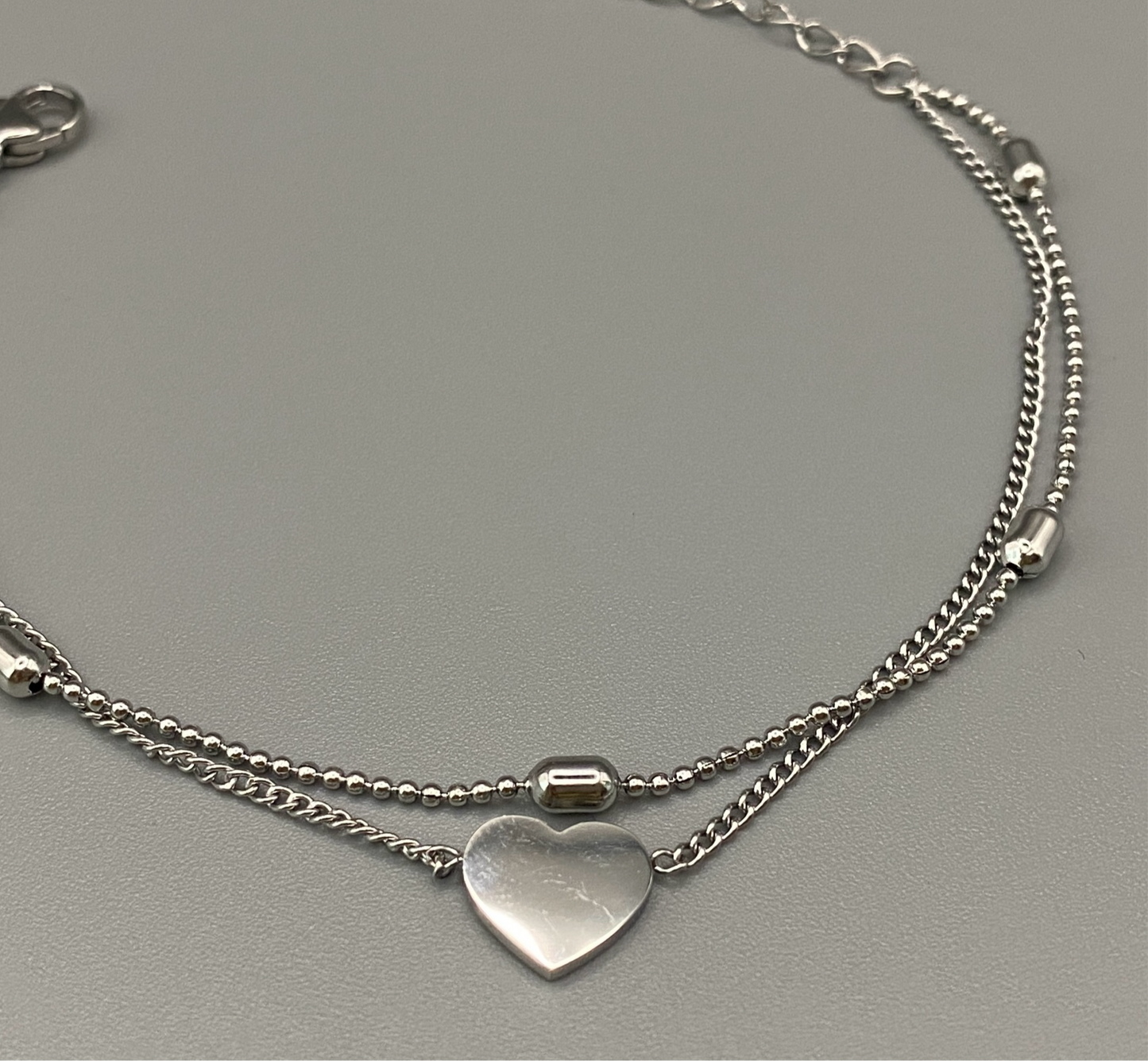“Cora Twin Chain Heart and Bead Bracelet in gold, featuring a romantic twin chain design with heart and bead accents. silver plated, made from durable titanium steel with PVD plating. Measures 17 cm with a 3 cm extender for adjustable fit.”
