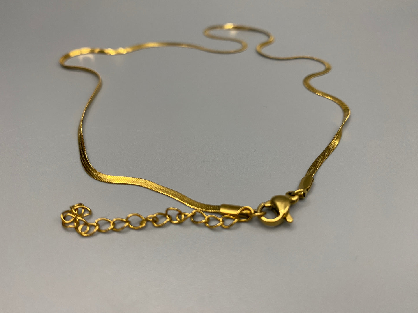 Dahlia Flat Snake Chain Gold Necklace. Sleek and modern design with a flat snake chain, perfect for adding elegance to any outfit. Key Features: Elegant Design: Flat snake chain with gold plating for a sophisticated look. Stainless Steel: Durable and tarnish-resistant. 18k Gold-Plated: Luxurious finish. Anti Tarnish & Waterproof: Maintains shine and luster over time. Size: 40 cm with a 5 cm extender for adjustable fit. Width: 2 mm for a delicate yet noticeable presence.