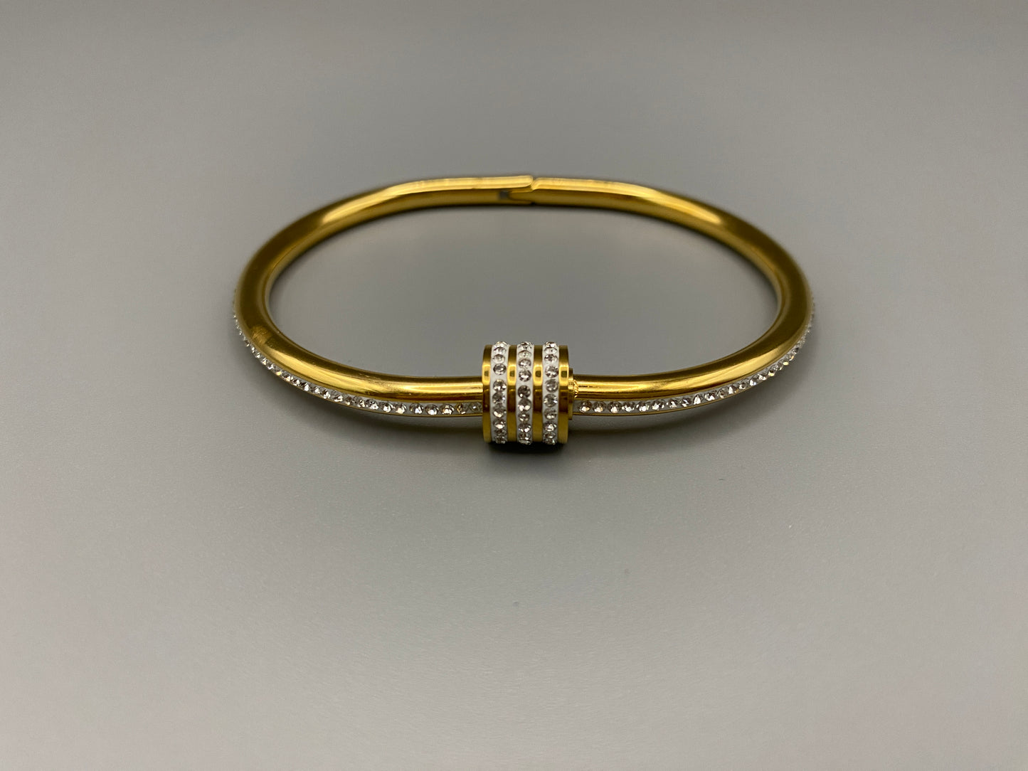“Eclipse Encrusted Bangle Bracelet in gold with an encrusted gem inlay, featuring 18K gold plating and a thread open and close mechanism for easy adjustment. Made from high-quality materials for long-lasting wear.”