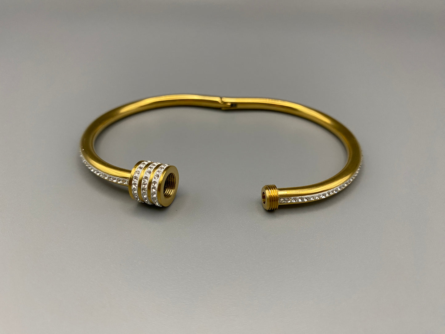 “Eclipse Encrusted Bangle Bracelet in gold with an encrusted gem inlay, featuring 18K gold plating and a thread open and close mechanism for easy adjustment. Made from high-quality materials for long-lasting wear.”