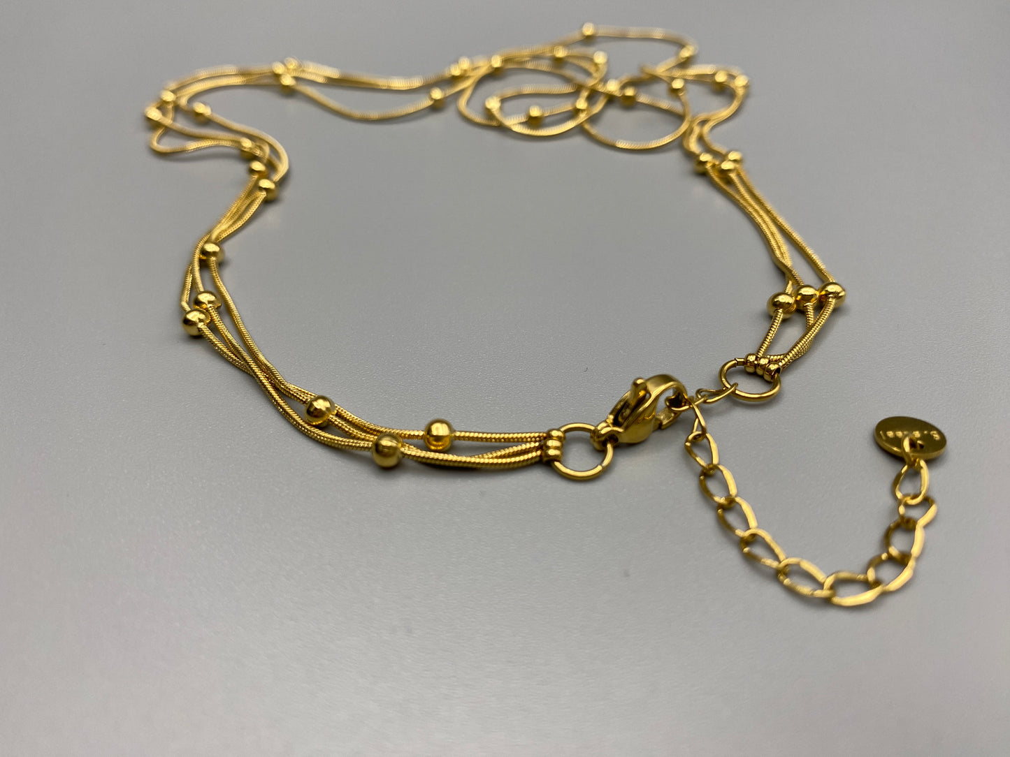 Freya Tri-Chain Bead Necklace Gold. Elegant tri-chain design with bead accents. 18k gold plated, PVD plated for durability. Adjustable length: 40 cm + 5 cm extender. Versatile for layering or solo wear.