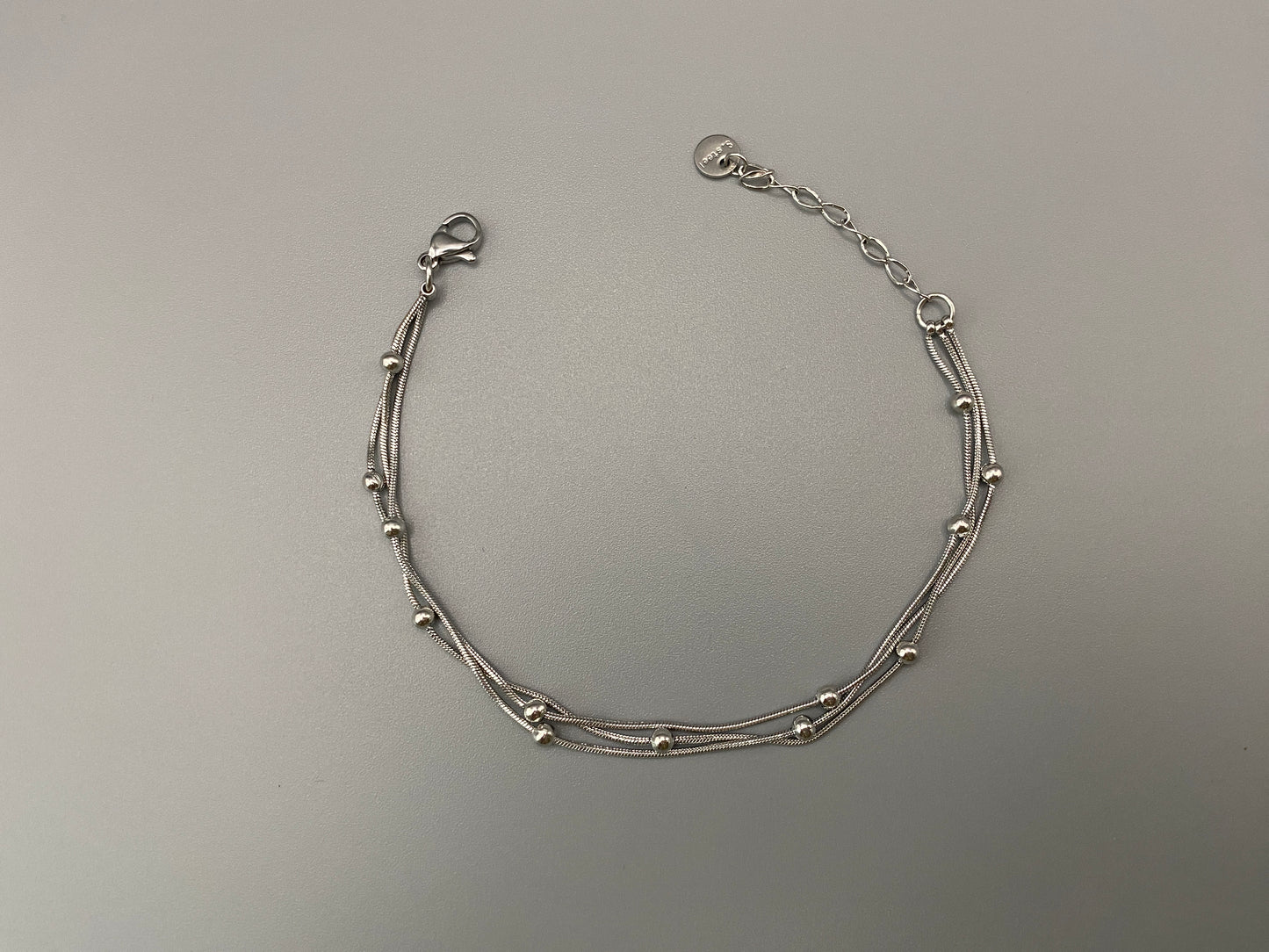 “Freya Tri-Chained Bead Bracelet in silver with three delicate chains and evenly spaced small beads. Silver plated, made from durable stainless steel with PVD plating. Measures 18 cm with a 3 cm extender for adjustable fit.”