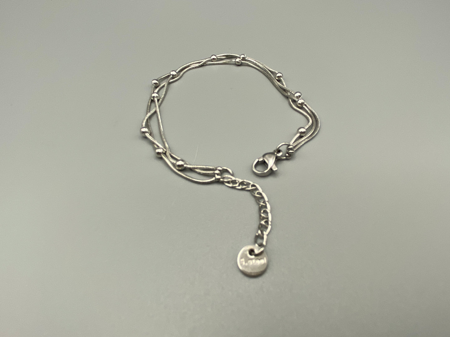 “Freya Tri-Chained Bead Bracelet in silver with three delicate chains and evenly spaced small beads. Silver plated, made from durable stainless steel with PVD plating. Measures 18 cm with a 3 cm extender for adjustable fit.”