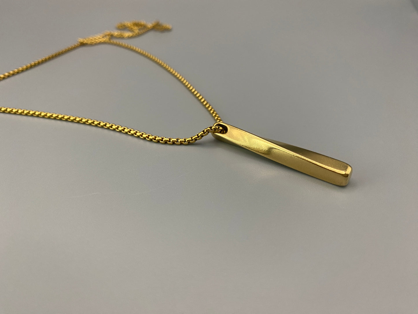 “Three stainless steel twist pendant necklaces in black gun plated, gold plated, and titanium plated finishes, displayed on a dark background. Each necklace features a geometric twist pendant on a link chain, suitable for