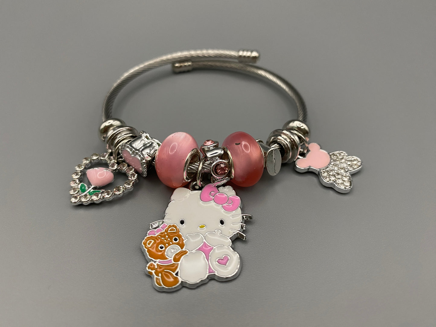Kitty Cartoon Character Bracelet in pink with stainless steel bangles, adorned with alloy charms, crystals, and glass beads. Features a charm with pink accents, combining playful elegance and sophistication.”
