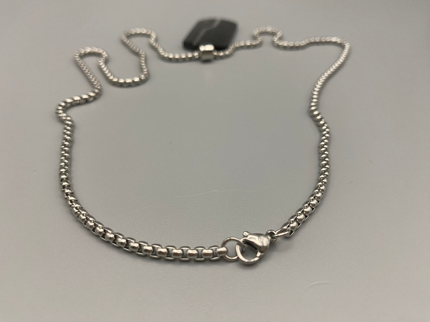 “Sentinel Black Pendant Stainless Steel Men’s Dog Necklace featuring a sleek black finish and a cross pattern, displayed on a strand chain.”