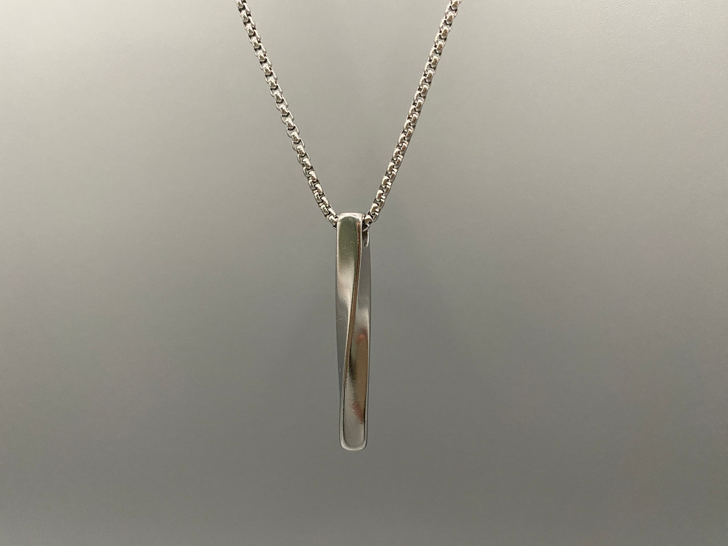 "Stainless steel twist pendant necklaces available in black gun plated, gold plated, and titanium plated finishes, displayed on a dark background. Each necklace features a geometric twist pendant on a link chain, suitable for unisex wear.”