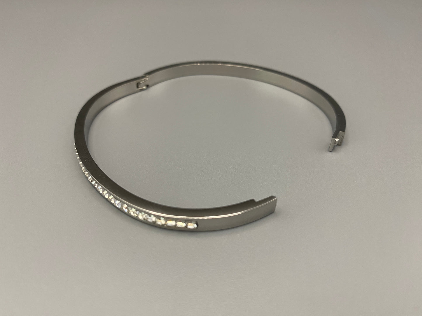“Simone Encrusted Bangle in silver with silver plating and gemstone inlay, offering a radiant and luxurious finish. Durable construction ensures long-lasting wear and tarnish resistance. Perfect for both everyday wear and special occasions.”