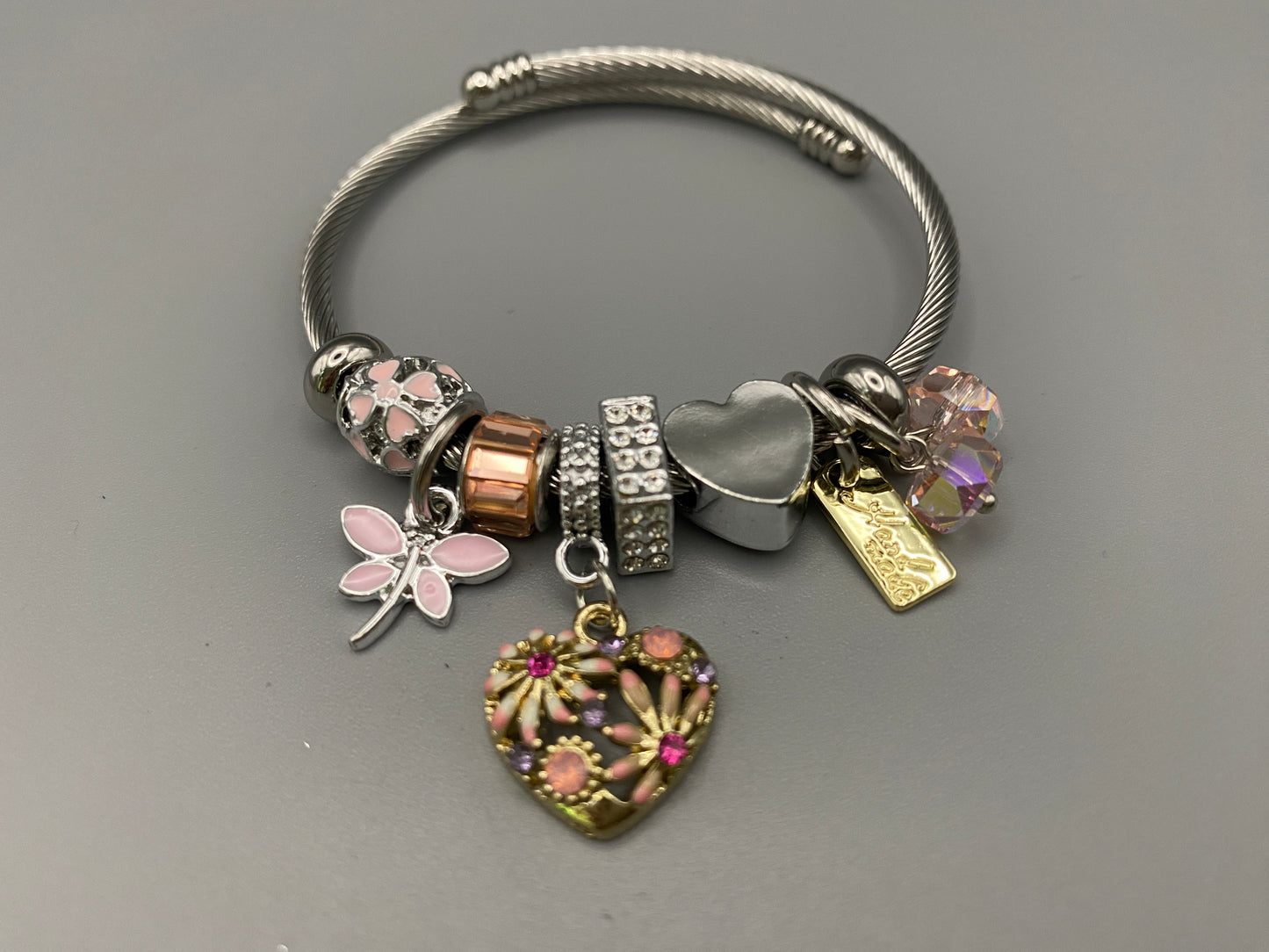 “Stellar Charm Bracelet in pink with playful charms including a heart, butterfly, and cube, crafted from high-quality stainless steel. Suitable for both women and kids, making it a perfect gift for any occasion.”