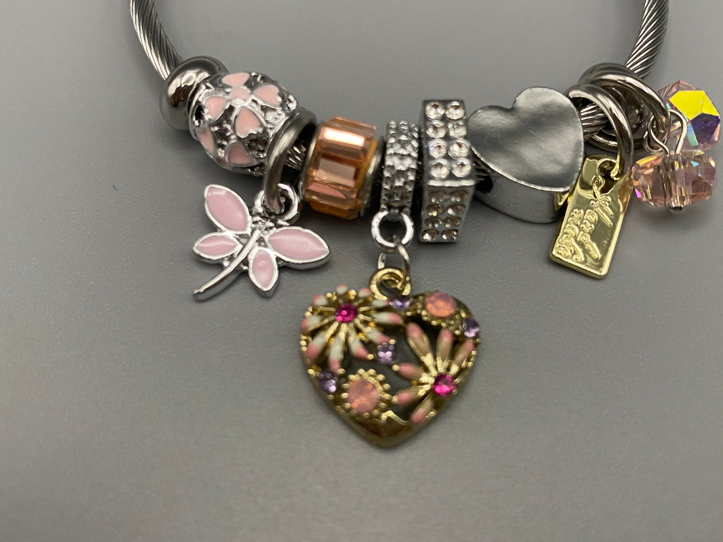 “Stellar Charm Bracelet in pink with playful charms including a heart, butterfly, and cube, crafted from high-quality stainless steel. Suitable for both women and kids, making it a perfect gift for any occasion.”