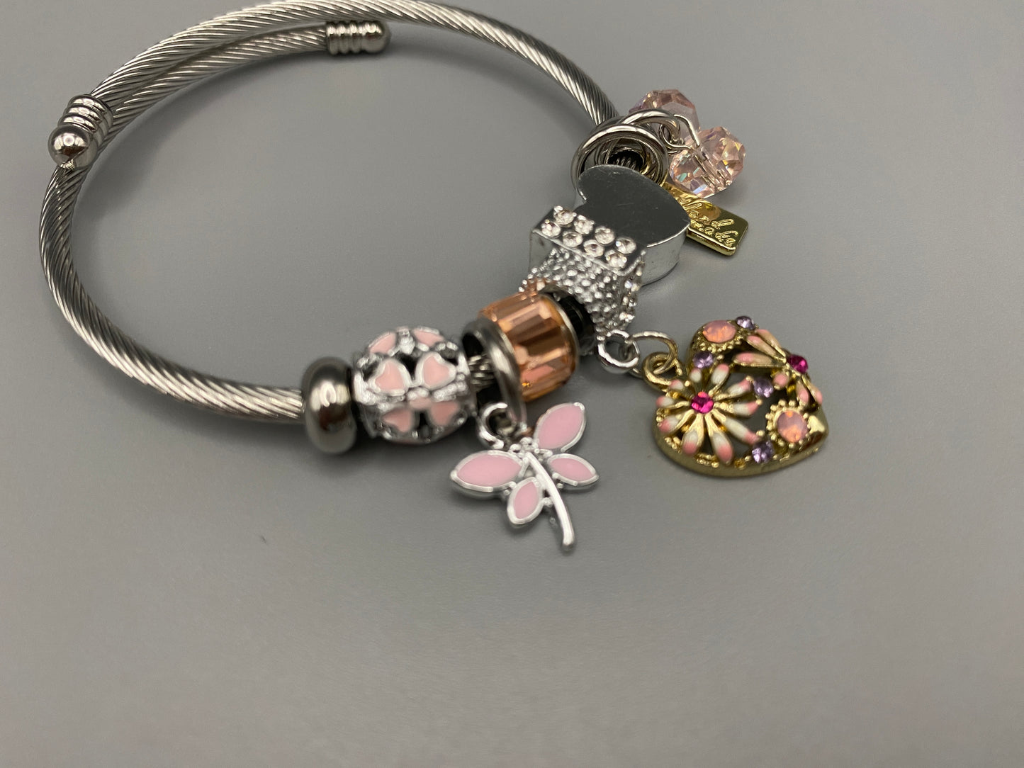 “Stellar Charm Bracelet in pink with playful charms including a heart, butterfly, and cube, crafted from high-quality stainless steel. Suitable for both women and kids, making it a perfect gift for any occasion.”