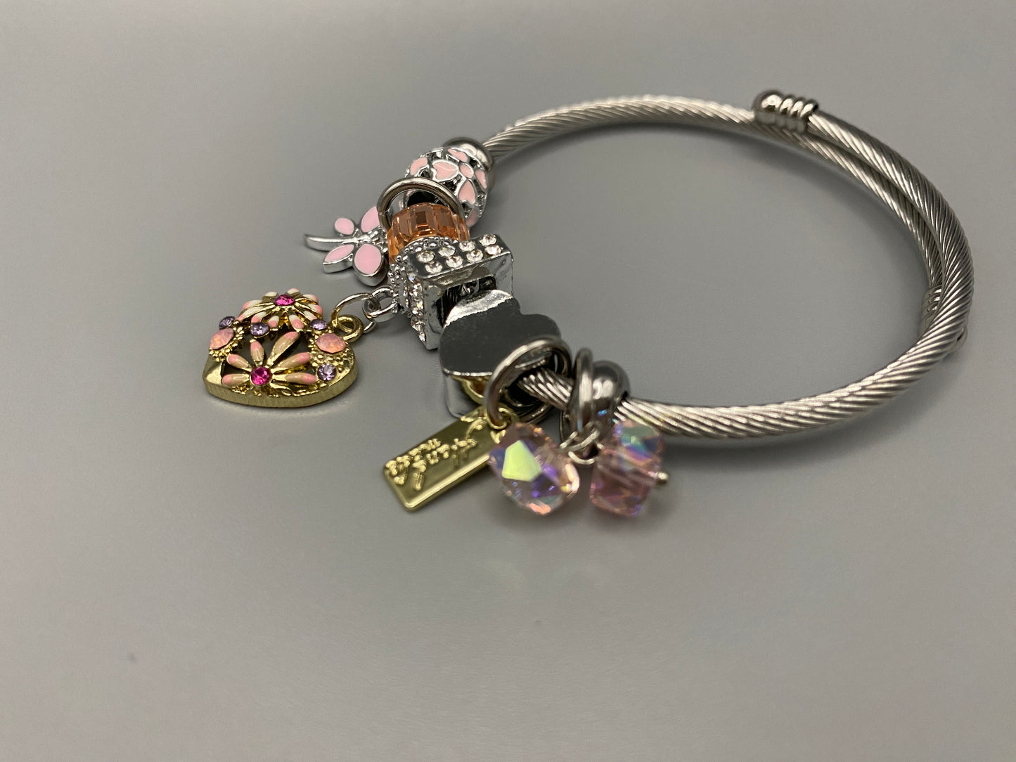 “Stellar Charm Bracelet in pink with playful charms including a heart, butterfly, and cube, crafted from high-quality stainless steel. Suitable for both women and kids, making it a perfect gift for any occasion.”