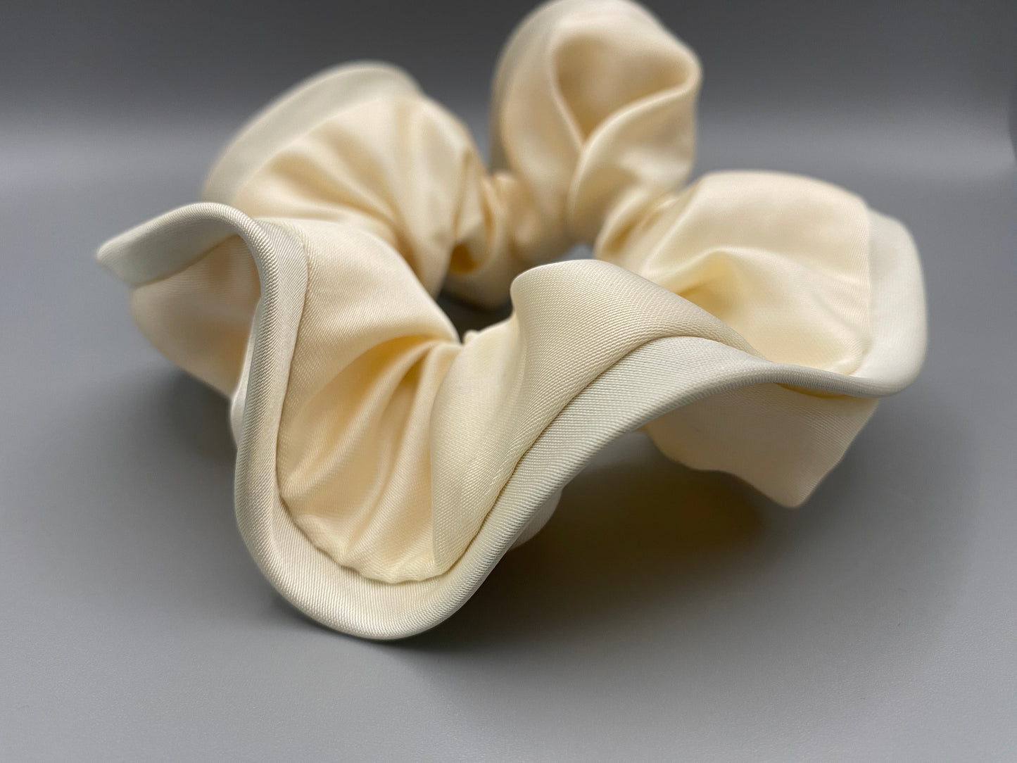“The Rebecca Flower Scrunchie in Cream, featuring a flower-shaped design made from durable and soft satin material. Measures 11 cm, perfect for creating voluminous and eye-catching hairdos. Chic and versatile, ideal for adding a touch of vintage elegance to any outfit.”