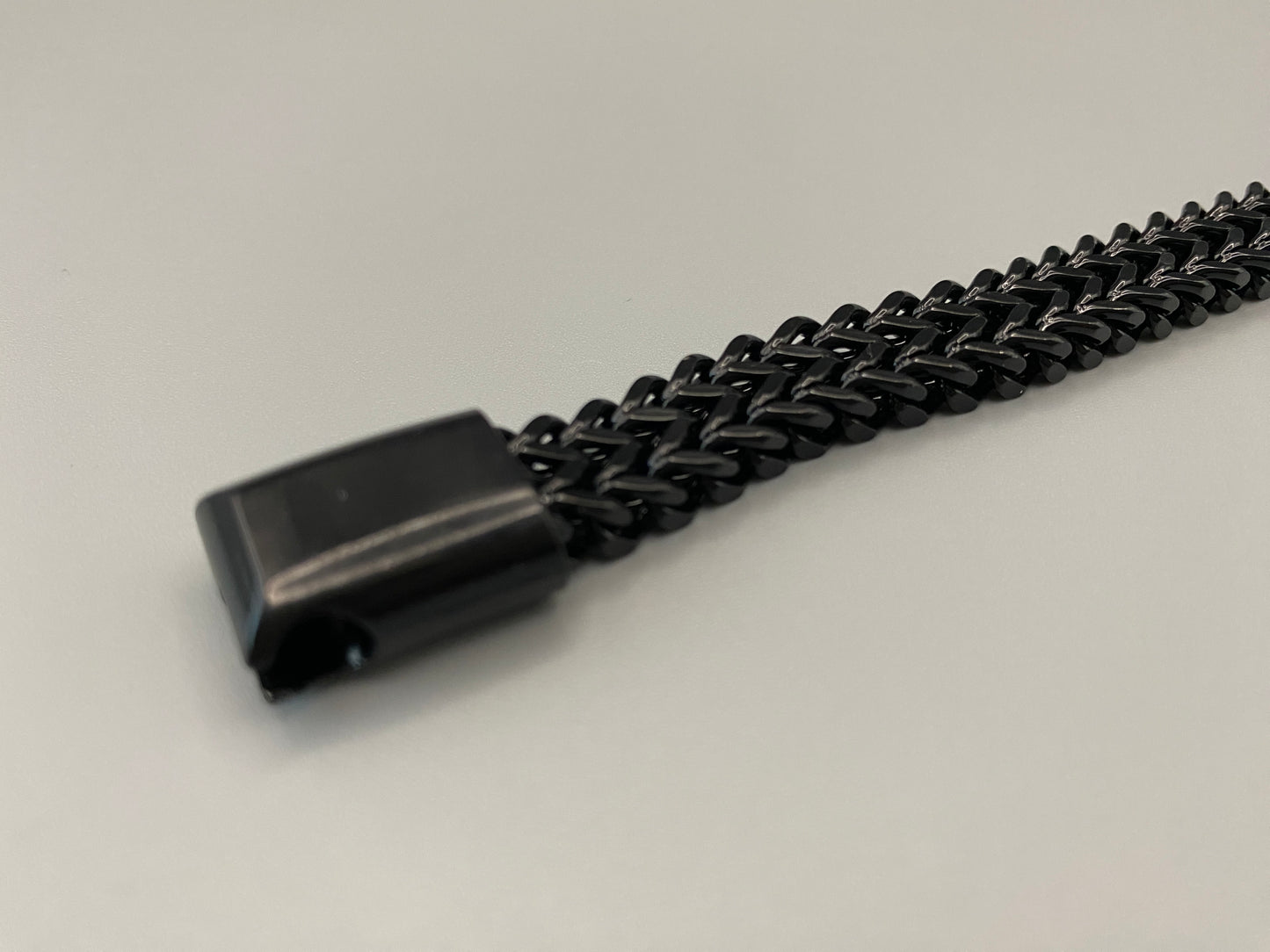 “A men’s bracelet with a chain and link design, made from shiny titanium steel. The bracelet features a geometric pattern and a smart magnet button clasp. It is available in silver, gold, and black colors, and measures 19-23 cm in length.”