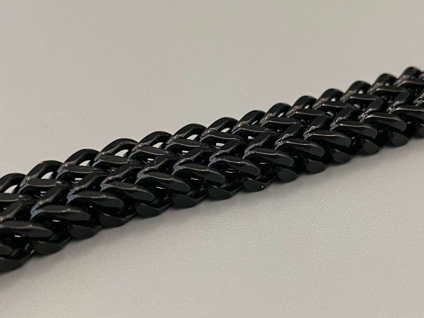 “A men’s bracelet with a chain and link design, made from shiny titanium steel. The bracelet features a geometric pattern and a smart magnet button clasp. It is available in silver, gold, and black colors, and measures 19-23 cm in length.”