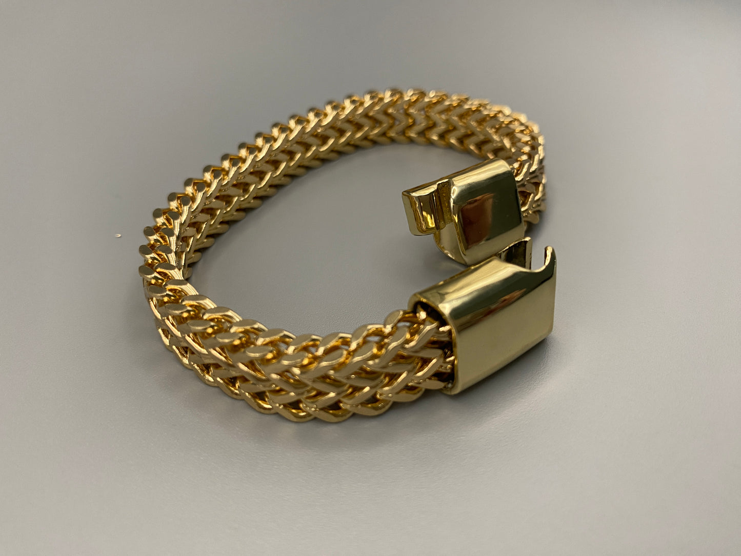 “A men’s bracelet with a chain and link design, made from shiny titanium steel. The bracelet features a geometric pattern and a smart magnet button clasp. It is available in silver, gold, and black colors, and measures 19-23 cm in length.”