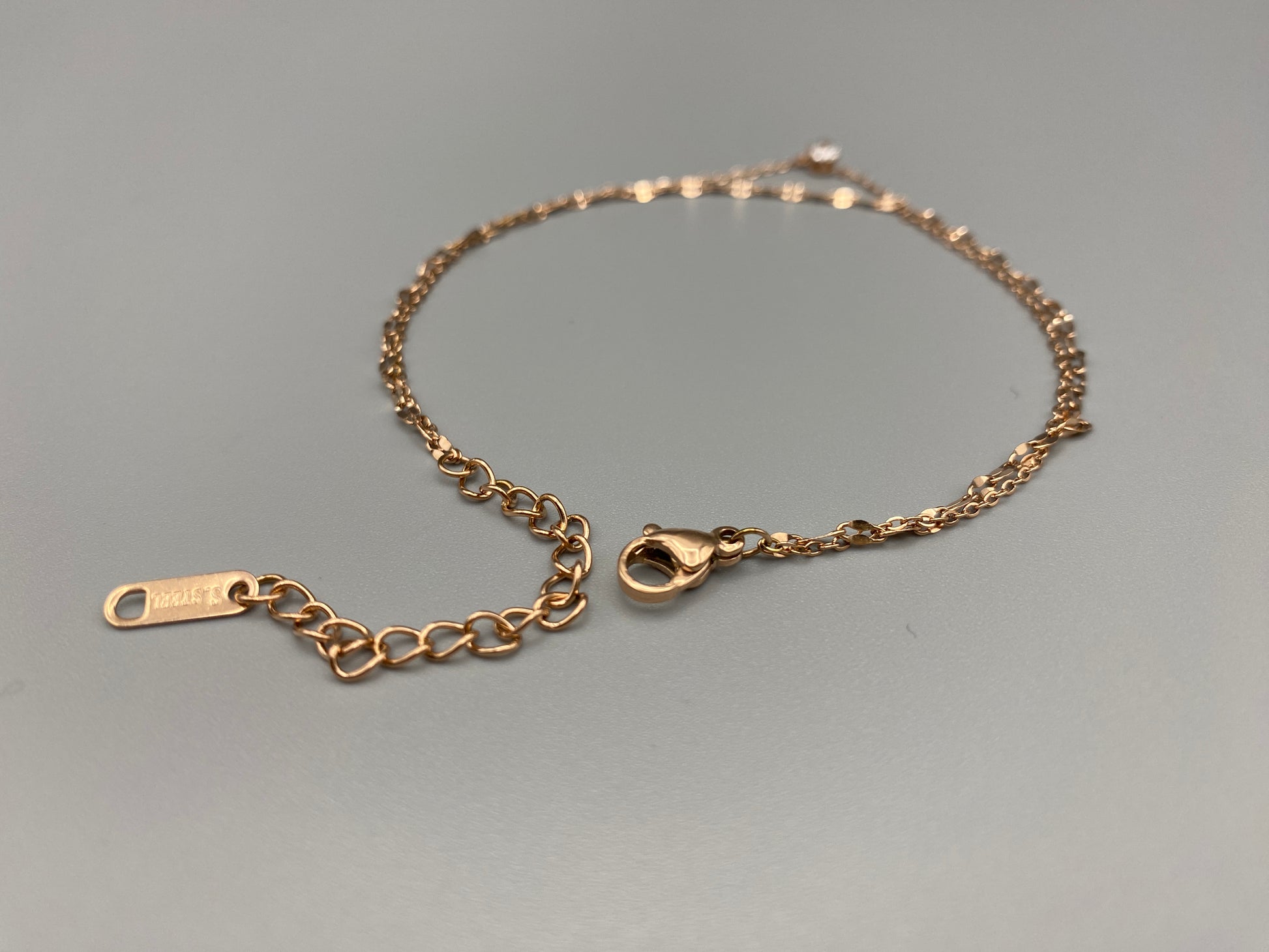 "Aurora Twin Chain Bracelet in rose gold features a sophisticated twin chain design adorned with zirconia gemstones. It is waterproof and measures 18 cm with a 3 cm extender for an adjustable fit."