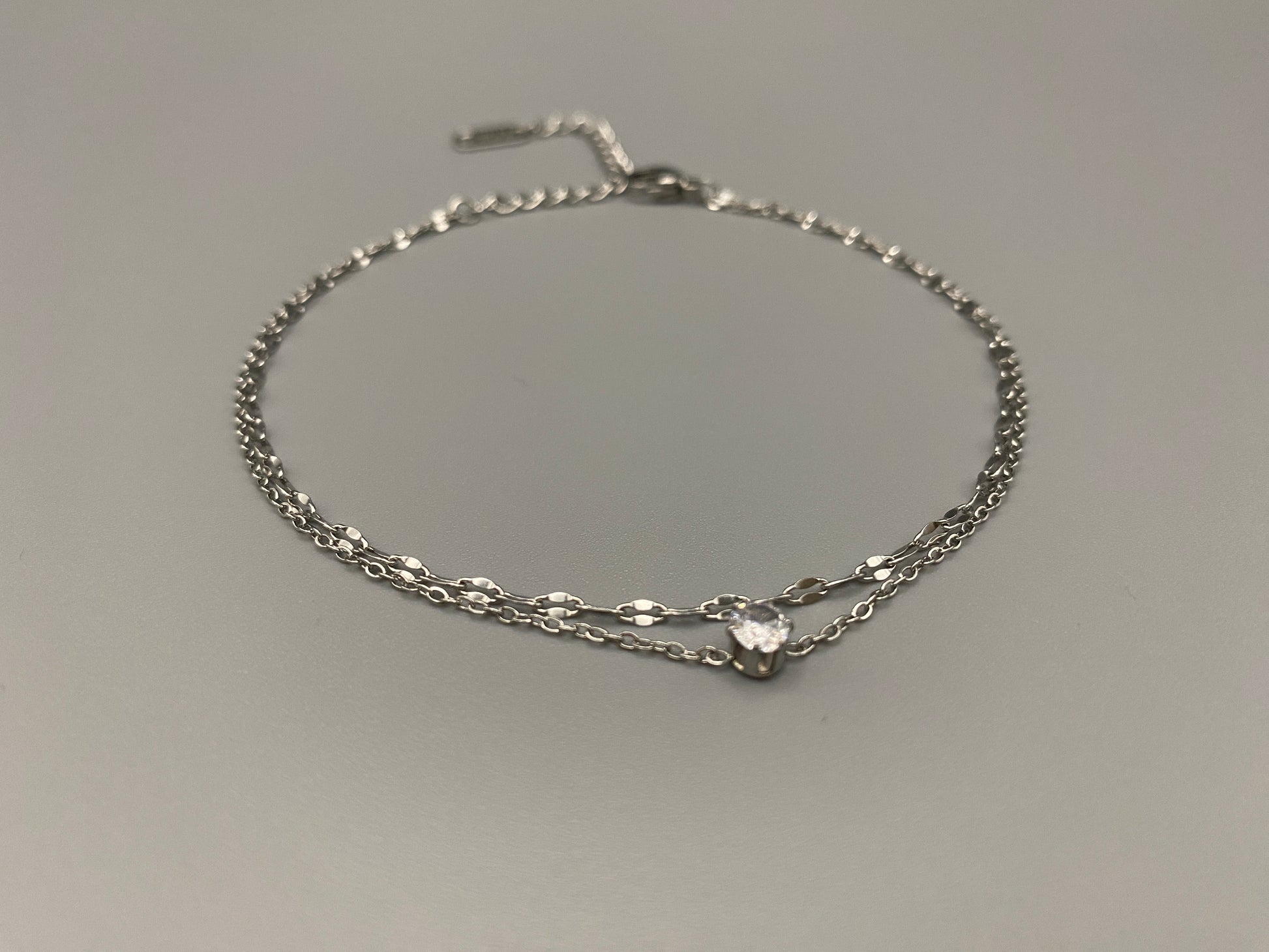 “Aurora Twin Chain Bracelet in silver with a sophisticated twin chain design, adorned with sparkling zirconia gemstones. Waterproof and measures 18 cm with a 3 cm extender for adjustable fit.”