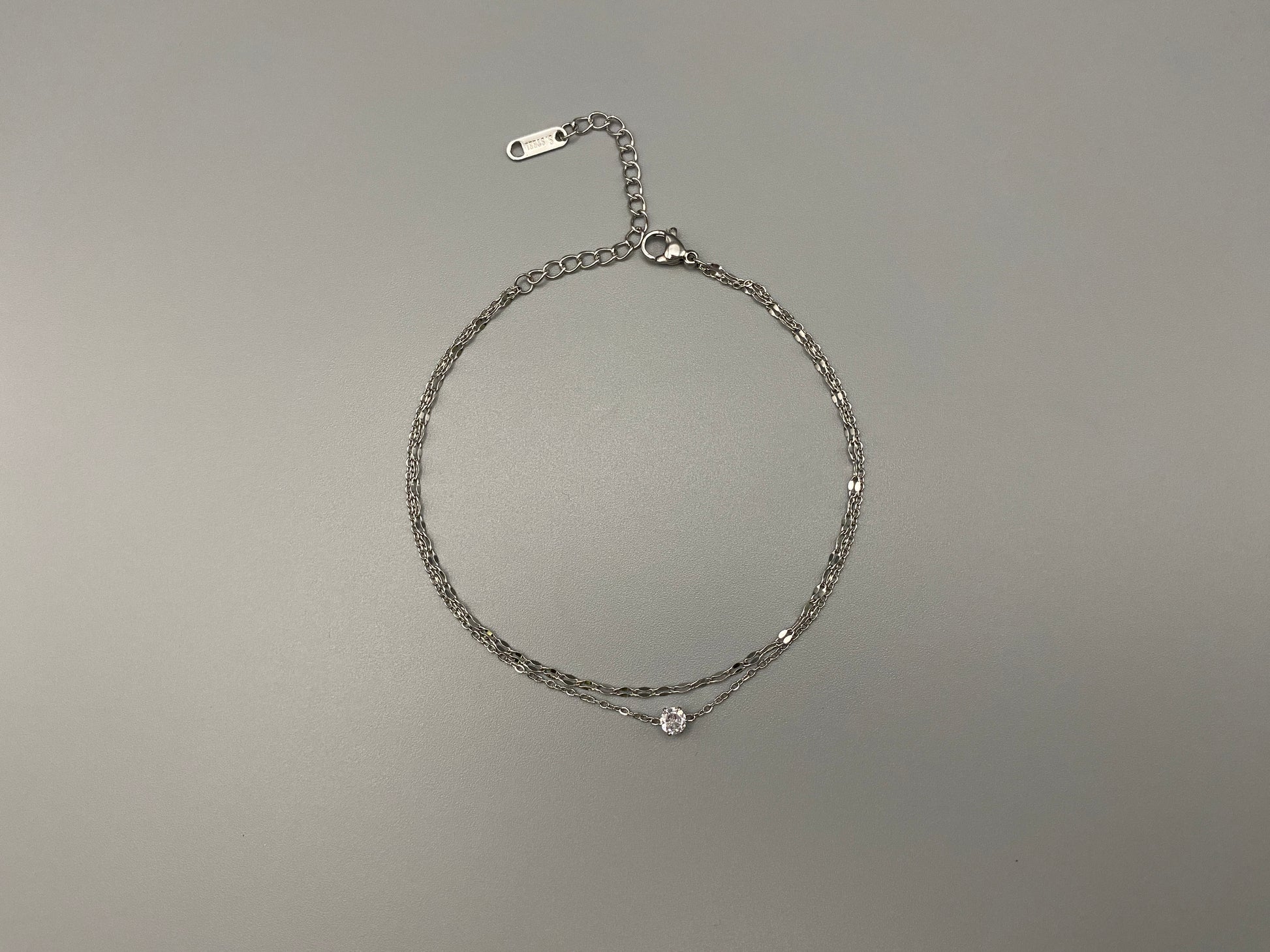 “Aurora Twin Chain Bracelet in silver with a sophisticated twin chain design, adorned with sparkling zirconia gemstones. Waterproof and measures 18 cm with a 3 cm extender for adjustable fit.”