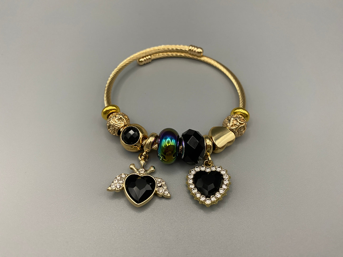 “Belle Black Charm Bracelet with gold-plated finish, featuring heart-cut crystals and rhinestones. Made from durable stainless steel with playful charms and micro insert inlay technology.”