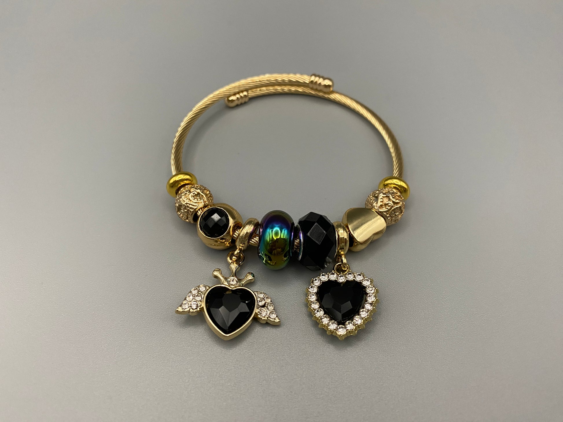 “Belle Black Charm Bracelet with gold-plated finish, featuring heart-cut crystals and rhinestones. Made from durable stainless steel with playful charms and micro insert inlay technology.”