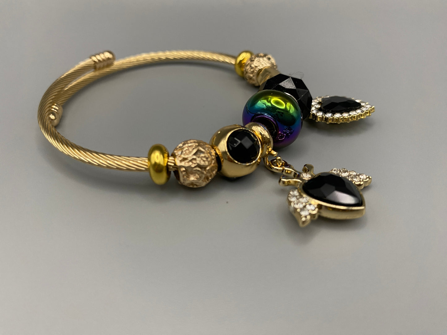 “Belle Black Charm Bracelet with gold-plated finish, featuring heart-cut crystals and rhinestones. Made from durable stainless steel with playful charms and micro insert inlay technology.”