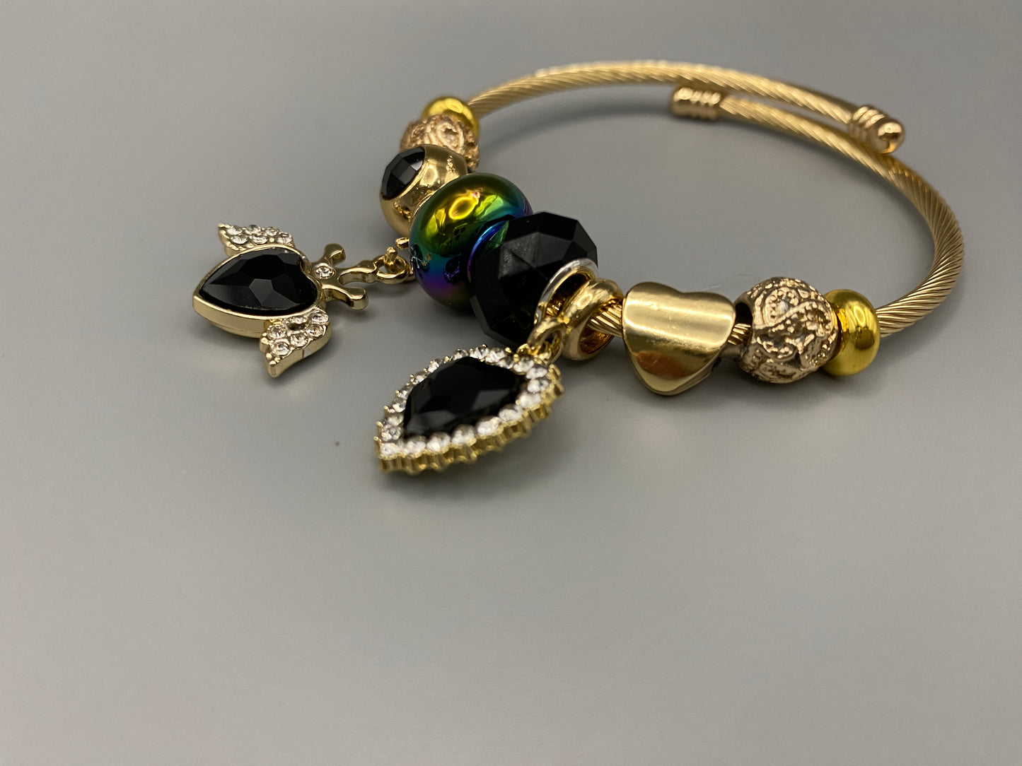 “Belle Black Charm Bracelet with gold-plated finish, featuring heart-cut crystals and rhinestones. Made from durable stainless steel with playful charms and micro insert inlay technology.”