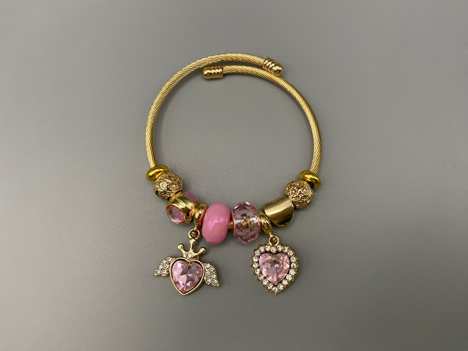 “Belle Pink Charm Bracelet with gold-plated finish, featuring heart-cut crystals and rhinestones. Made from durable stainless steel with playful charms and micro insert inlay technology.”