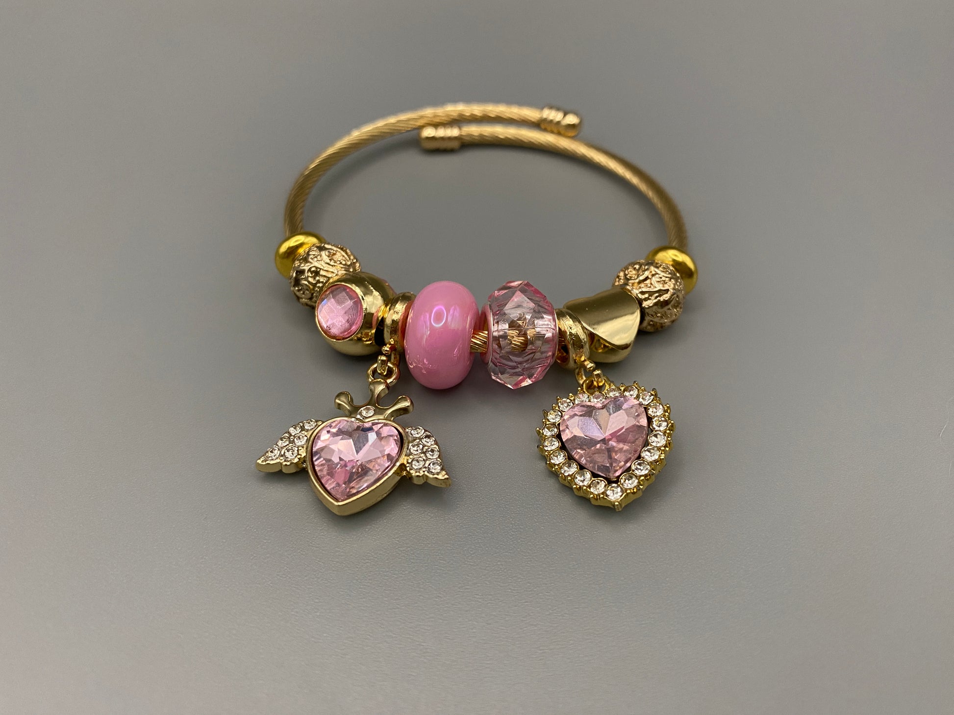 “Belle Pink Charm Bracelet with gold-plated finish, featuring heart-cut crystals and rhinestones. Made from durable stainless steel with playful charms and micro insert inlay technology.”